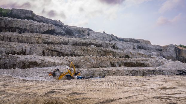 A quarry with excavators working on rocky terrain under a cloudy sky.
